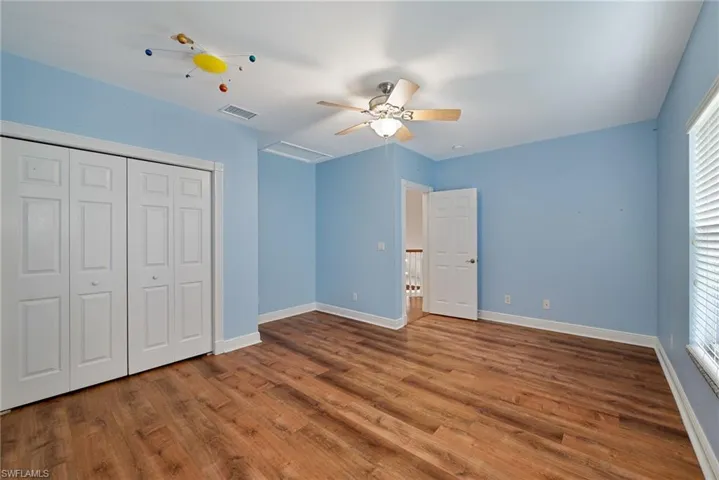 One of two upstairs guest bedrooms with a closet, wood finished floors, and a ceiling fan