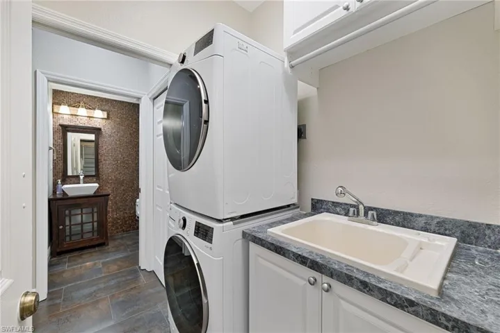 Laundry room featuring cabinet space, stone tile flooring, and stacked washer and clothes dryer