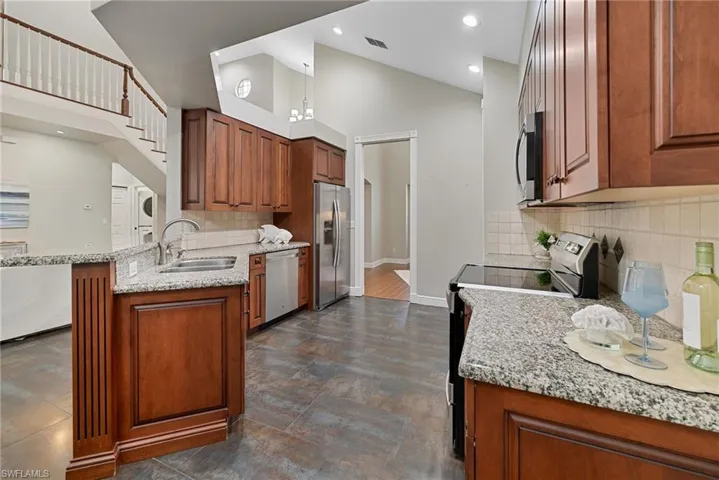 Kitchen featuring wood finish cabinetry, stainless steel appliances, light stone counters, lofted ceiling, and a peninsula