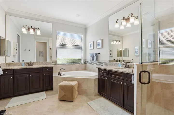 Bathroom featuring a garden tub, a shower stall, two vanities, crown molding, and suspended lighting