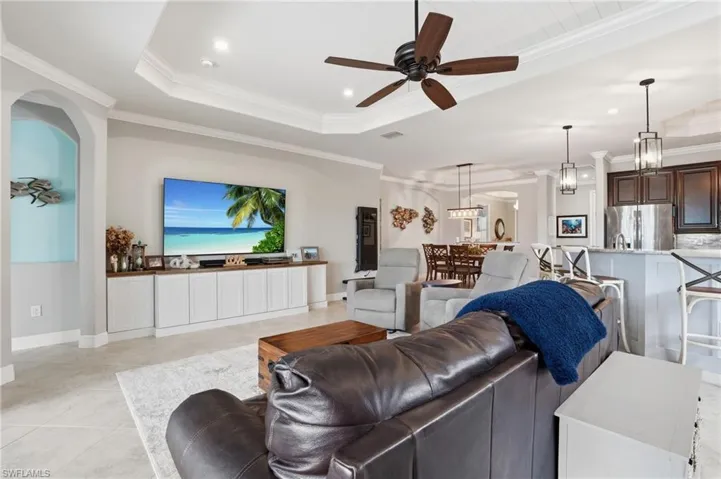 Living area with a raised ceiling, crown molding, ceiling fan, and recessed lighting