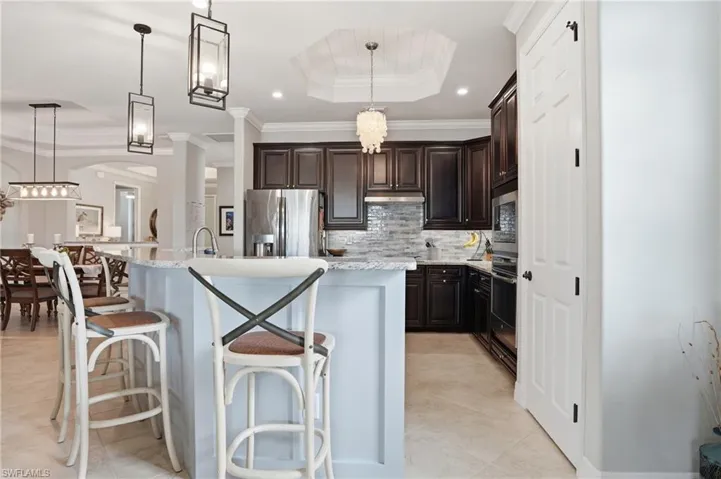 Kitchen with a raised ceiling, dark wood finish cabinets, a kitchen breakfast bar, decorative backsplash, and crown molding