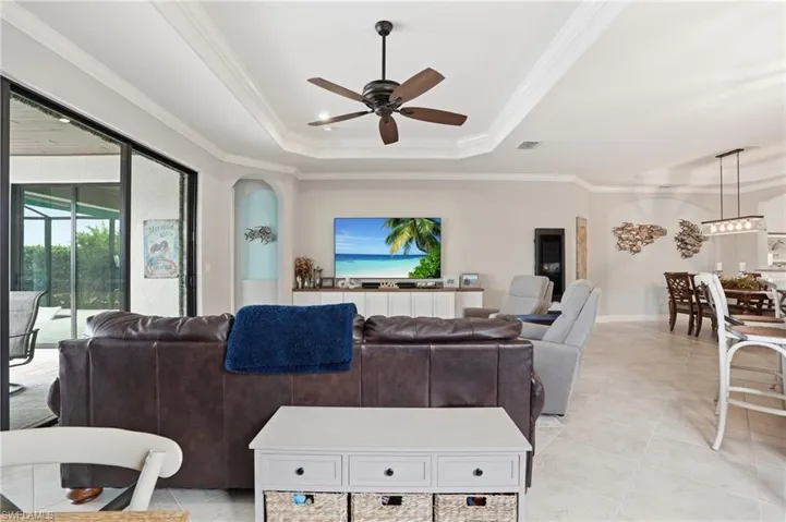 Living area with crown molding, a ceiling fan, a tray ceiling, and light tile patterned flooring