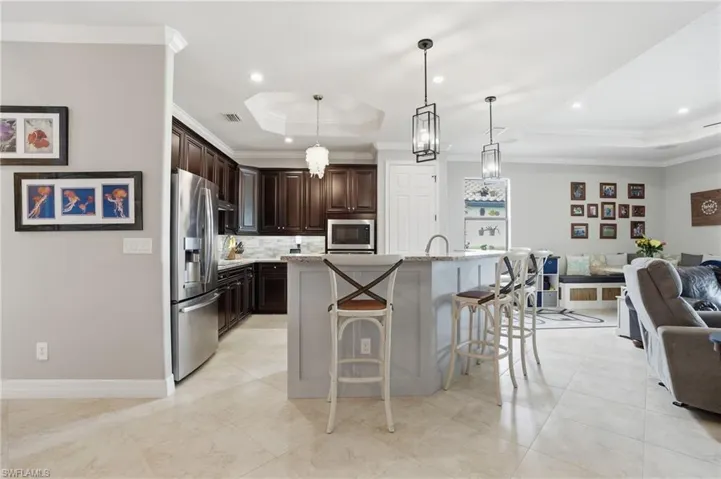 Kitchen featuring open floor plan, a tray ceiling, ornamental molding, dark wood finish cabinetry, and stainless steel appliances