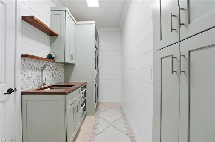 Laundry room featuring cabinet space, wooden walls, light tile patterned floors, crown molding, and stacked washer / drying machine