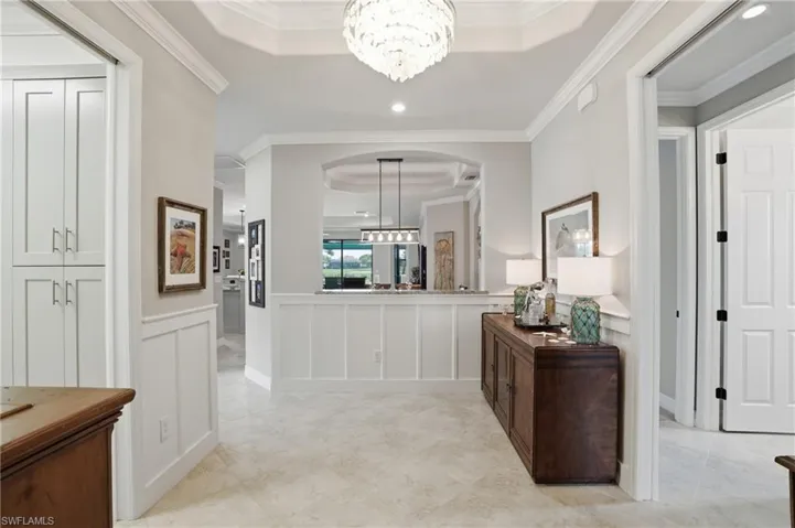 Hallway with hanging lights, a tray ceiling, a wainscoted wall, crown molding, and a decorative wall