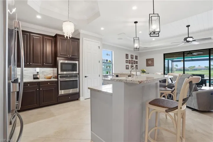 Kitchen featuring a raised ceiling, light stone countertops, dark wood finish cabinetry, stainless steel appliances, and a ceiling fan