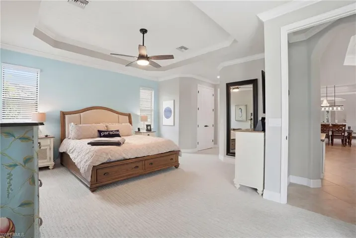 Bedroom featuring multiple windows, light colored carpet, a raised ceiling, a ceiling fan, and ornamental molding