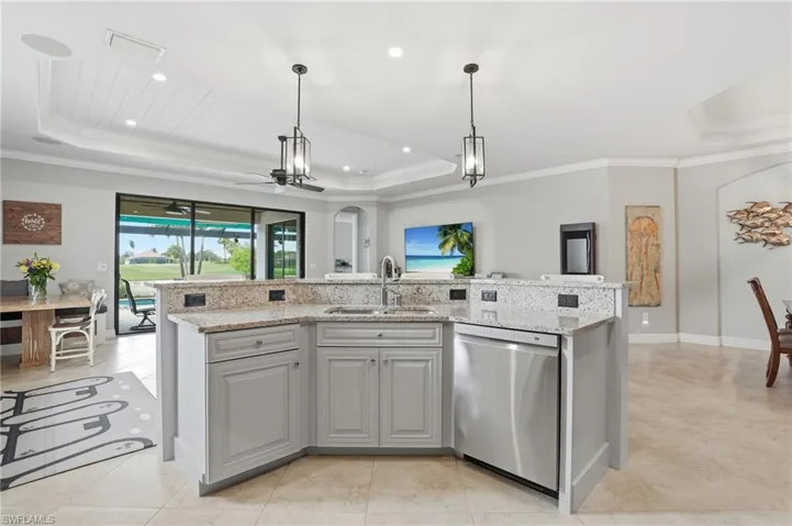 Kitchen with a tray ceiling, stainless steel dishwasher, a center island with sink, light stone counters, and a ceiling fan