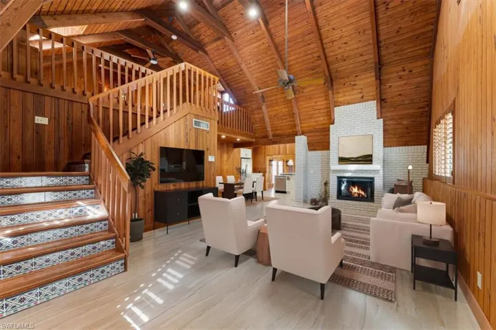 Living area featuring wood walls, a wood ceiling with exposed beams, high vaulted ceiling, ceiling fan, and a fireplace