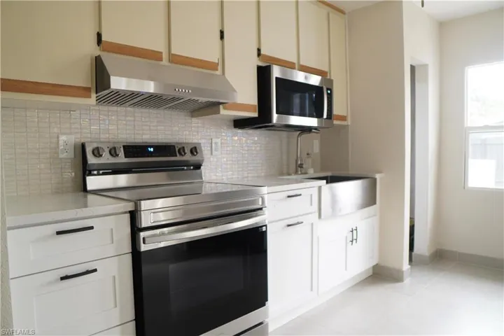 Kitchen with stainless steel appliances, under cabinet range hood, backsplash, light stone counters, and light tile patterned floors
