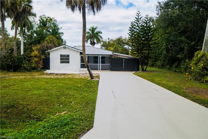 Ranch-style house featuring a front lawn, driveway, a metal roof, and a carport