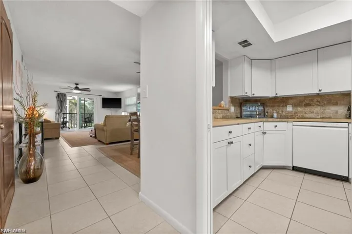 Kitchen with light tile patterned floors, dishwasher, white cabinetry, and backsplash