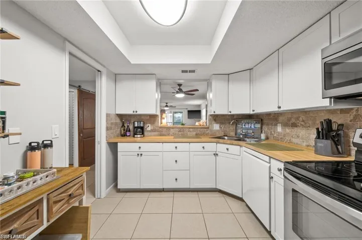 Kitchen featuring stainless steel appliances, white cabinetry, wood counters, and light tile patterned floors