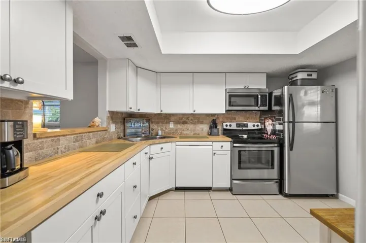 Kitchen featuring stainless steel appliances, white cabinetry, butcher block counters, light tile patterned floors, and a tray ceiling