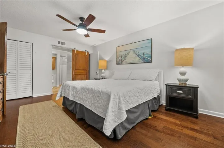 Bedroom with a barn door, dark wood-style floors, a closet, ceiling fan, and a textured ceiling