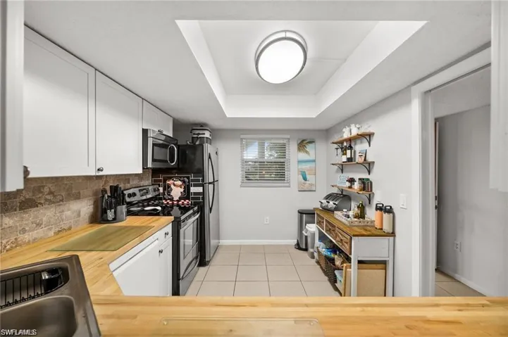 Kitchen with appliances with stainless steel finishes, white cabinets, light tile patterned floors, butcher block countertops, and decorative backsplash