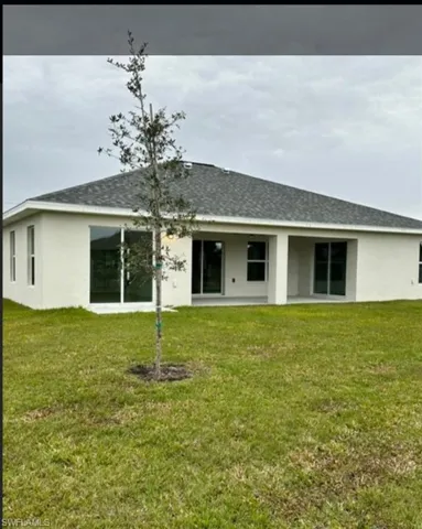 Rear view of house featuring stucco siding, a patio area, roof with shingles, and a lawn