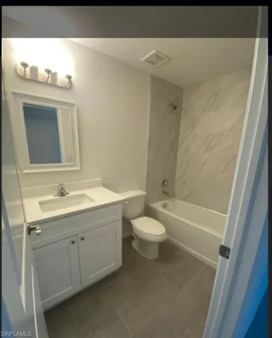 Bathroom featuring vanity, shower / tub combination, and dark tile patterned floors