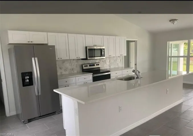 Kitchen with stainless steel appliances, white cabinetry, lofted ceiling, a large island, and light stone countertops