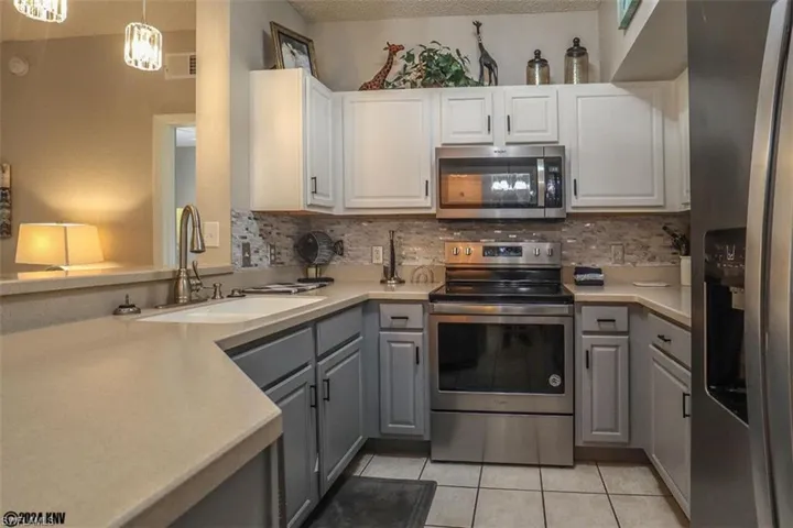 Kitchen with stainless steel appliances, gray cabinetry, light tile patterned floors, backsplash, and a textured ceiling