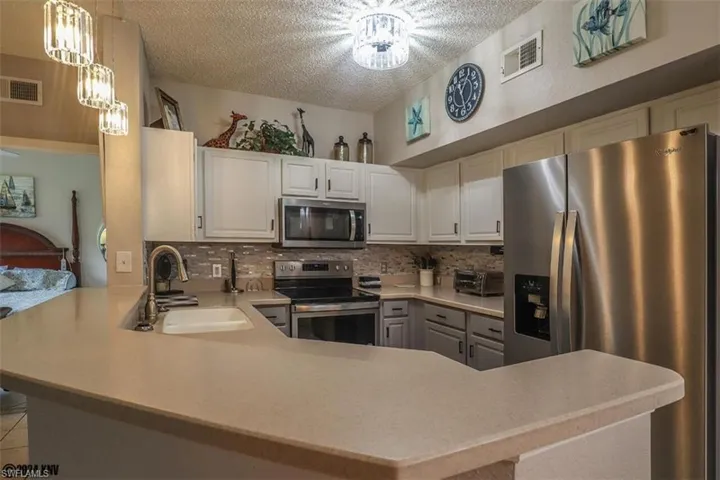 Kitchen with stainless steel appliances, a textured ceiling, tasteful backsplash, a peninsula, and light countertops