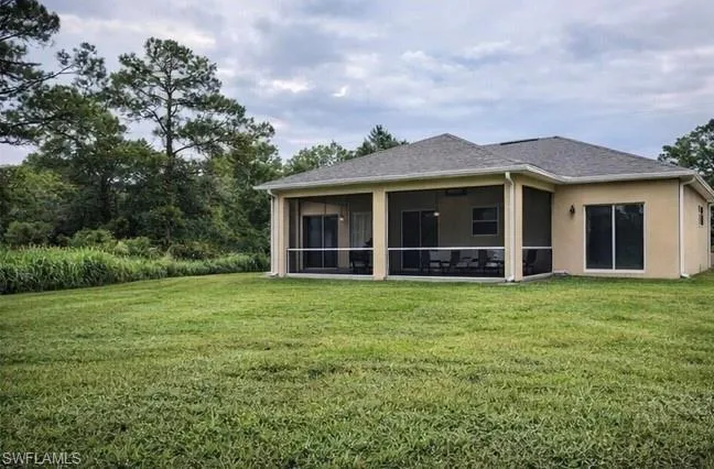 Back of property featuring a lawn, stucco siding, a sunroom, and a shingled roof