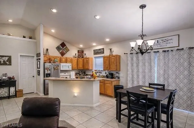 Kitchen featuring vaulted ceiling, hanging lights, light countertops, white appliances, and wood finish cabinetry