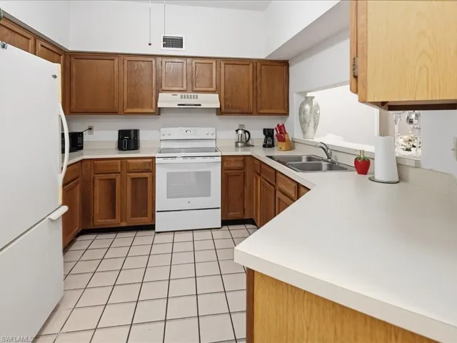 Kitchen with white appliances, brown cabinets, light countertops, and under cabinet range hood
