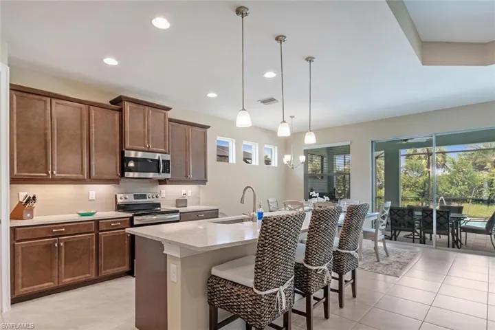 Kitchen featuring stainless steel appliances, a center island with sink, hanging light fixtures, sink, and light tile floors