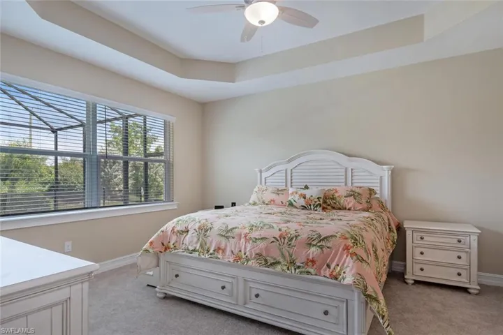 Bedroom with ceiling fan, light colored carpet, and a raised ceiling