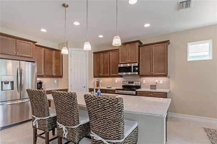 Kitchen featuring a center island with sink, appliances with stainless steel finishes, decorative light fixtures, tasteful backsplash, and light tile flooring
