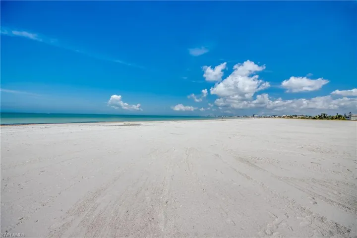 Expansive sandy beach with a clear blue sky, featuring distant coastal structures and calm turquoise waters
