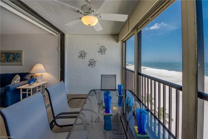 Enclosed balcony with glass paneling and a ceiling fan, offering expansive beachfront and ocean scenery
