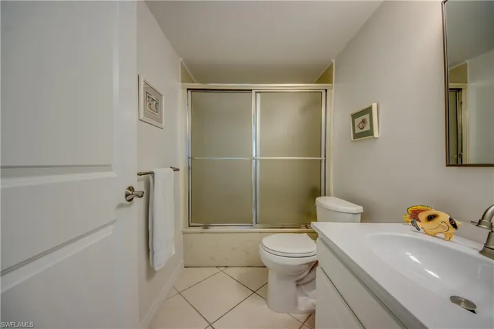 Full bathroom featuring a white vanity with an integrated sink, brushed nickel faucet, a toilet, and a bathtub with frosted glass sliding doors