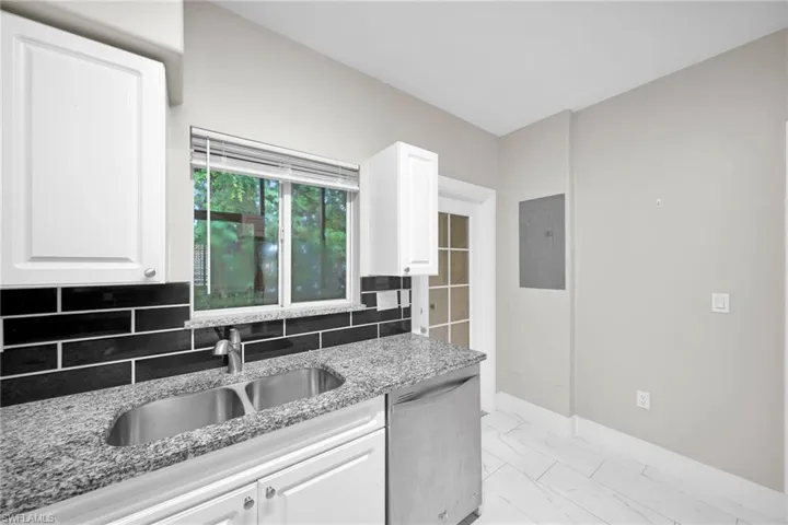 Kitchen with stainless steel dishwasher, white cabinetry, light stone countertops, and electric panel