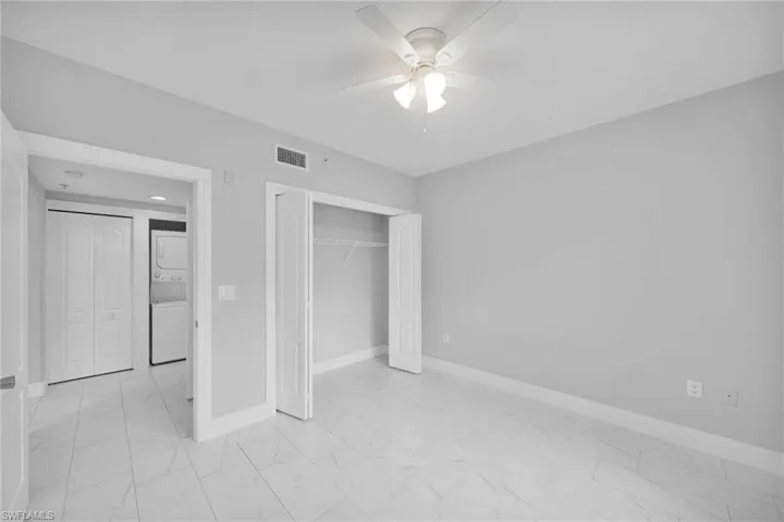 Unfurnished bedroom featuring stacked washer / dryer, a closet, ceiling fan, and light tile patterned floors
