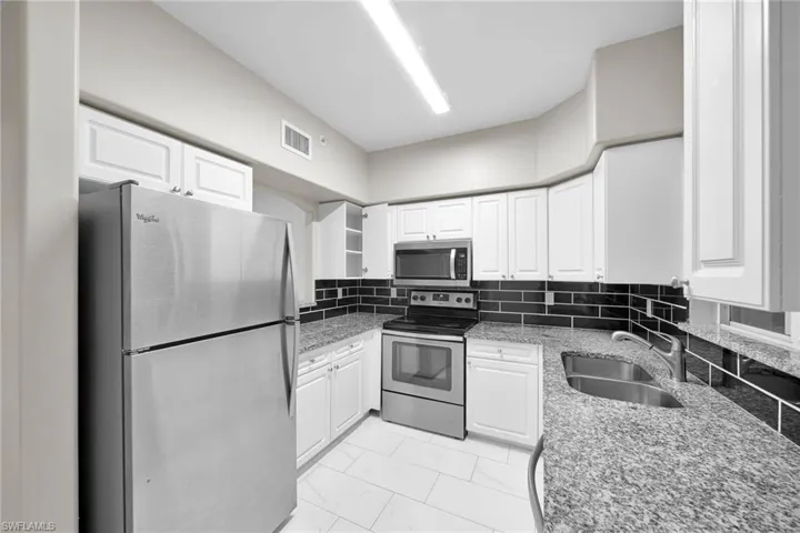 Kitchen with appliances with stainless steel finishes, light tile patterned floors, white cabinets, and sink