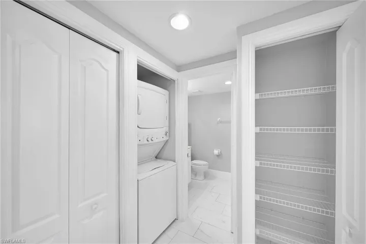 Clothes washing area with stacked washer and clothes dryer and light tile patterned floors