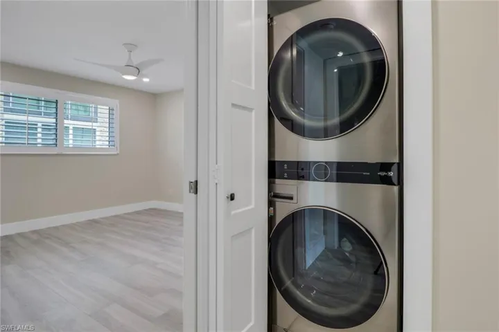 Laundry area featuring stacked washer and dryer, ceiling fan, and wood finished floors