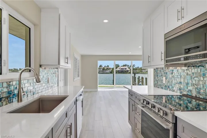 Two tone kitchen featuring stainless steel appliances, light stone countertops, recessed lighting, backsplash, and light wood finished floors