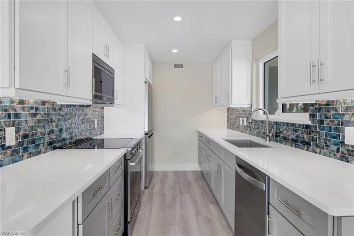 Kitchen with stainless steel appliances, two tone cabinetry, light wood-type flooring, light stone counters, and recessed lighting