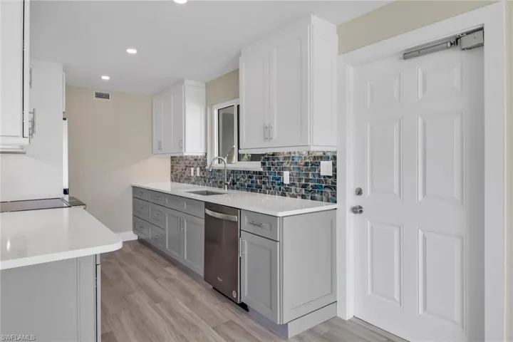 Kitchen with two tone cabinets, light stone counters, stainless steel dishwasher, light wood-type flooring, and recessed lighting
