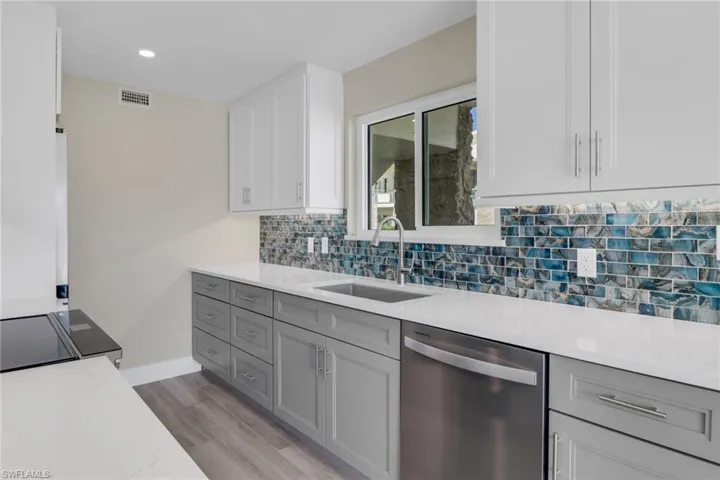 Kitchen with dual tone cabinets, dishwasher, light stone counters, light wood-style floors, and black electric range oven