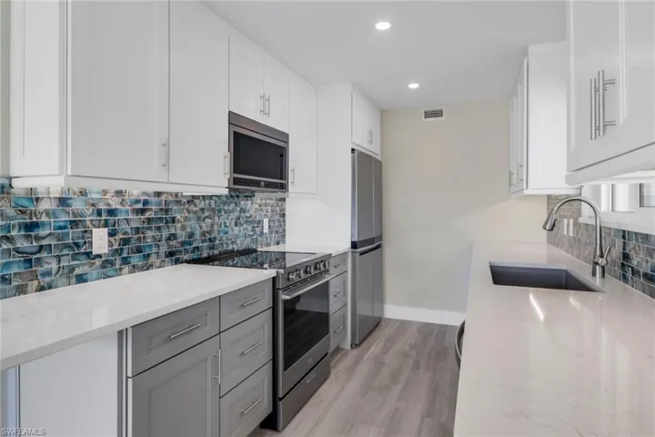 Kitchen with stainless steel appliances, tasteful backsplash, light stone counters, dual tone cabinets, and light wood-type flooring