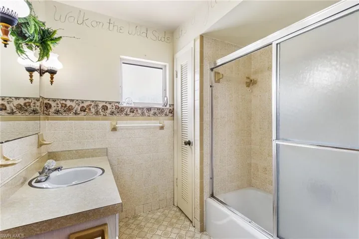Bathroom featuring tile walls, enclosed tub / shower combo, and vanity