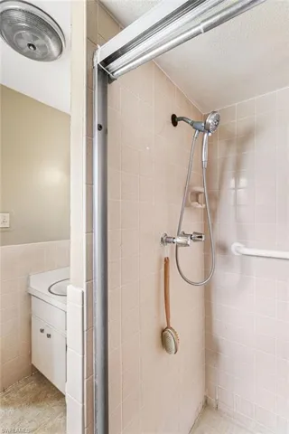 Bathroom with tile walls, vanity, a tile shower, and a textured ceiling