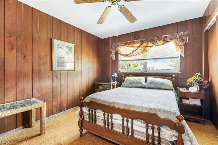 Carpeted bedroom with wood walls and ceiling fan