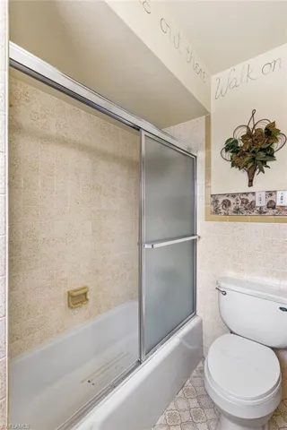 Bathroom featuring toilet, tile walls, and enclosed tub / shower combo