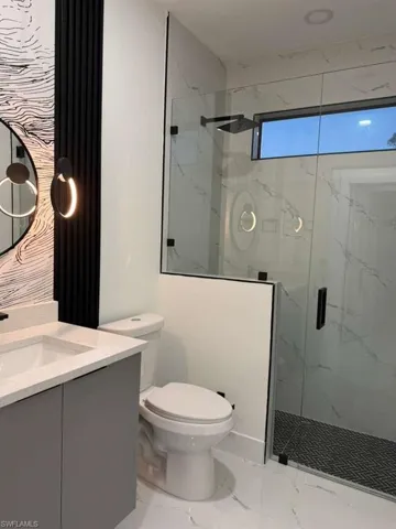 Bathroom featuring vanity, a marble finish shower, and light marble finish flooring